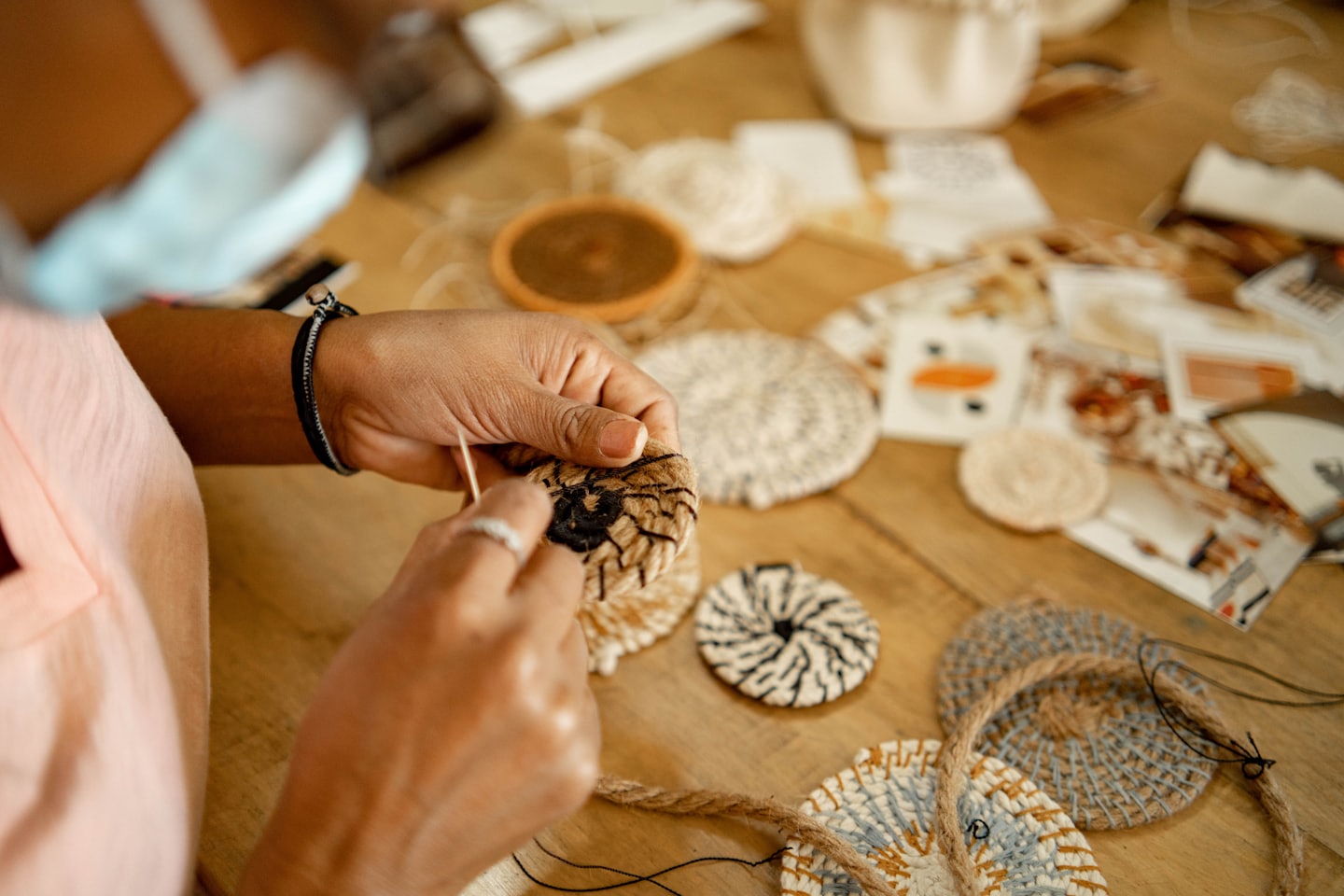 Mani che intrecciano un piccolo oggetto circolare con fibre naturali e un ago.